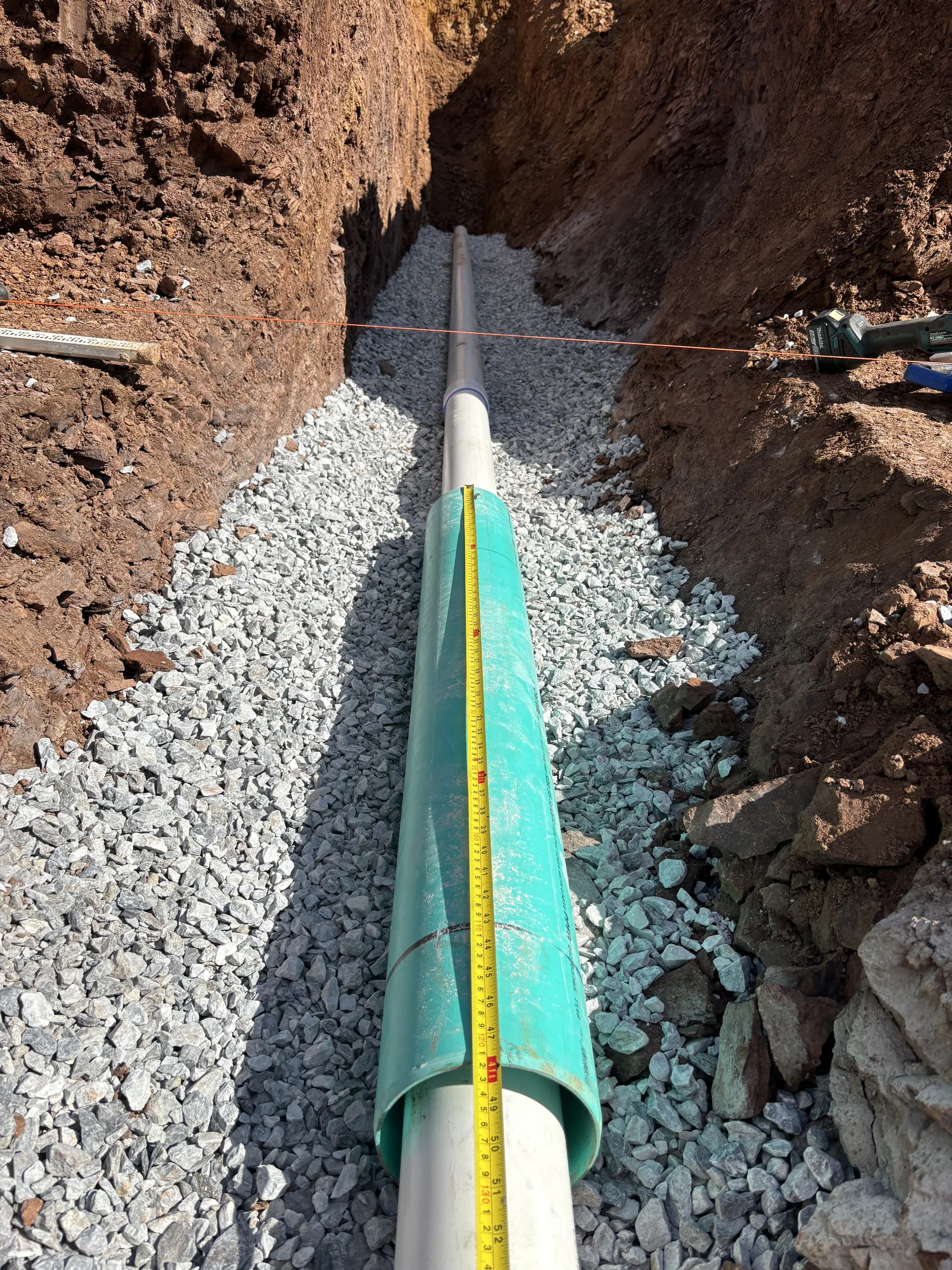 Large green PVC sewer pipe seated in a gravel-bedded trench